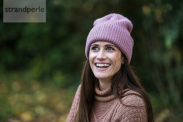 Porträt einer schönen Frau mit rosa Strickmütze  die im Freien steht und lächelt
