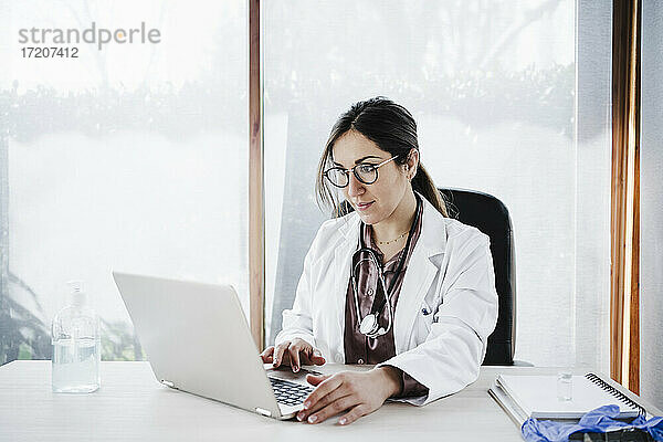 Weibliches medizinisches Fachwissen bei der Benutzung eines Laptops  während sie im Krankenhaus am Fenster sitzt