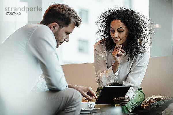 Geschäftsfrau  die mit einem Kollegen an einem digitalen Tablet arbeitet  während sie in einem Café sitzt