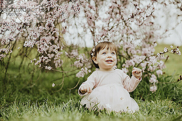 Baby Mädchen sitzt auf Gras in der Nähe von Kirschbaum im Frühling