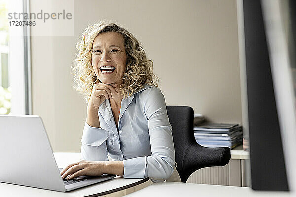 Lachende Geschäftsfrau mit Laptop im Büro sitzend