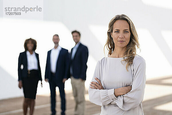 Selbstbewusste Geschäftsfrau  die auf einer Büroterrasse mit Kollegen im Hintergrund steht und starrt