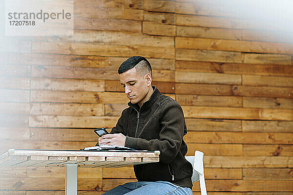 Junger männlicher Unternehmer  der in einem Straßencafé sitzt und sein Smartphone benutzt