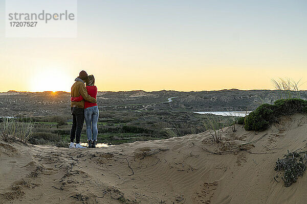 Junges Paar mit Blick auf den Sonnenuntergang auf einer Sanddüne stehend