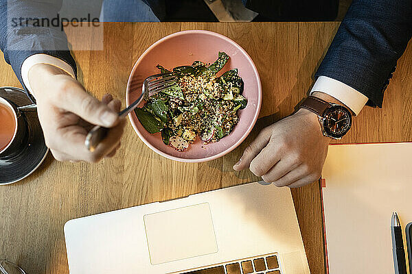 Mann isst Salat am Laptop auf dem Tisch im Cafe
