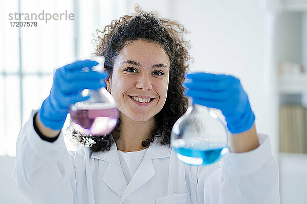Lächelnde Wissenschaftlerin  die eine chemische Lösung in einem Becherglas in einer Klinik testet