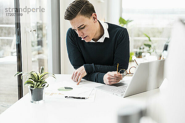 Konzentrierter männlicher Berufstätiger  der ein Dokument liest  während er im Büro zu Hause sitzt