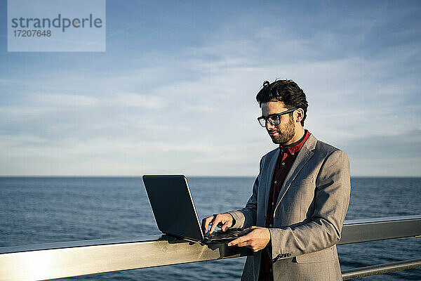 Geschäftsmann mit Laptop auf dem Geländer am Meer