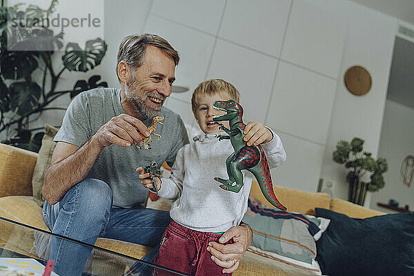 Vater und Sohn spielen mit Dinosaurier-Spielzeug im Wohnzimmer