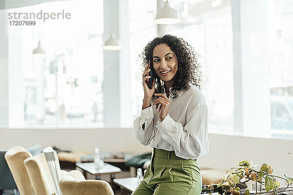 Junge Geschäftsfrau  die mit ihrem Handy telefoniert  während sie in einem Café am Tisch sitzt