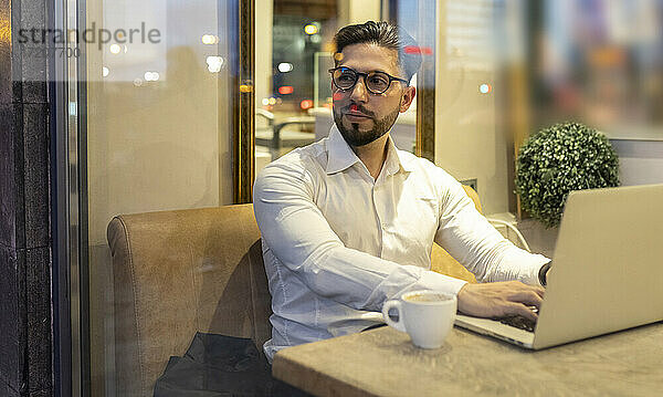 Männlicher Unternehmer schaut weg  während er einen Laptop in einem Café benutzt