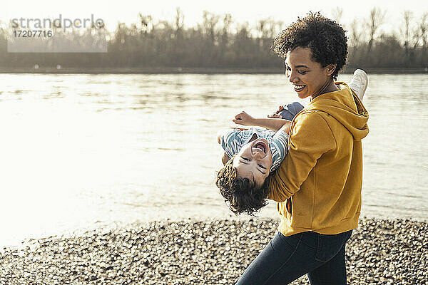 Lächelnde Mutter mit fröhlichem Jungen auf dem Arm am See