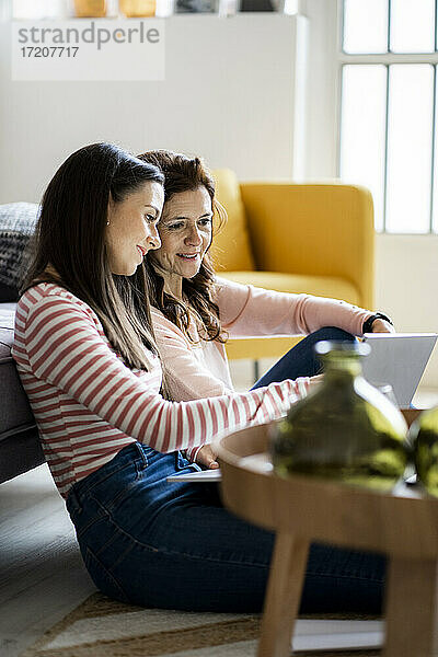 Lächelnde Mutter und Tochter schauen auf den Laptop  während sie zu Hause im Wohnzimmer sitzen