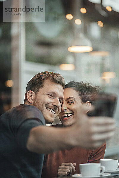 Glückliches Paar nimmt Selfie durch Handy beim Sitzen im Café