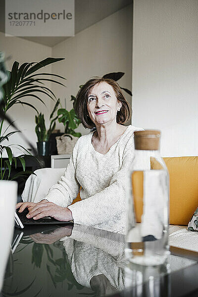 Lächelnde Frau schaut weg  während sie zu Hause einen Laptop benutzt