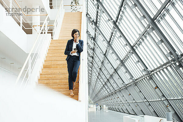 Unternehmerin mit Smartphone auf einer Treppe im Flur stehend