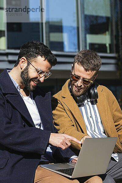 Lächelnde Geschäftsleute  die im Freien sitzend am Laptop arbeiten