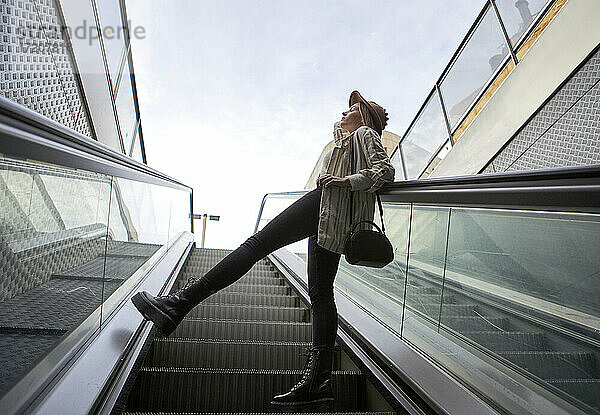 Frau lehnt sich auf der Rolltreppe an ein Geländer und steht gegen den Himmel