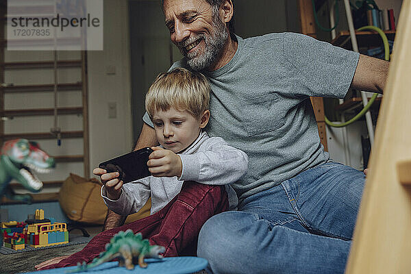 Vater beobachtet Sohn beim Spielen von Spielen auf dem Smartphone zu Hause