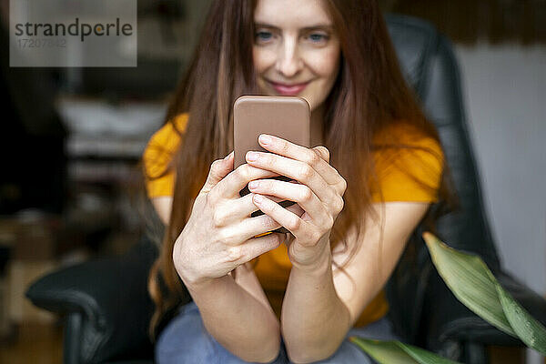 Schöne Frau hält Smartphone  während sie auf einem Stuhl zu Hause sitzt