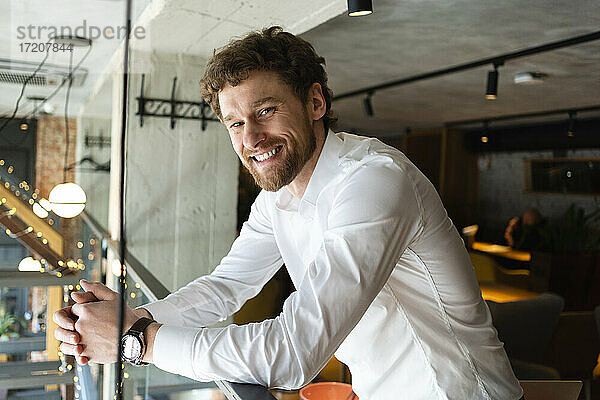 Lächelnder Geschäftsmann lehnt am Geländer eines Cafés