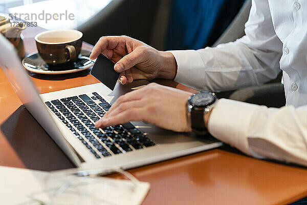 Mann hält Kreditkarte für Online-Zahlung über Laptop im Café
