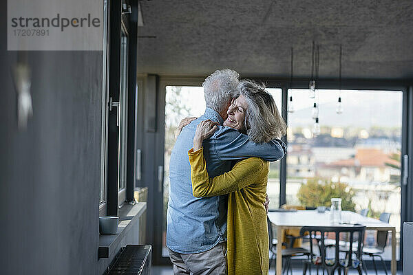 Ältere Frau lächelt  während sie einen Mann zu Hause umarmt