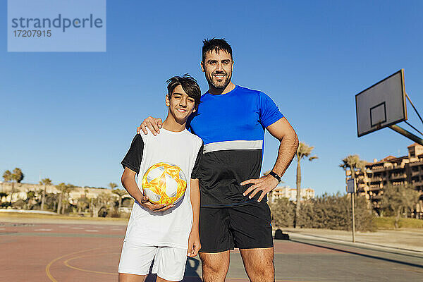 Lächelnder Vater mit Hand auf der Schulter seines Sohnes auf dem Sportplatz