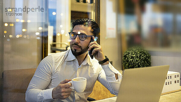 Geschäftsmann spricht mit seinem Smartphone und hält eine Kaffeetasse in einem Café