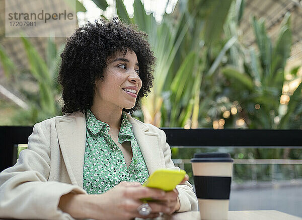 Nachdenkliche Frau  die ein Smartphone benutzt  während sie in einem Café sitzt