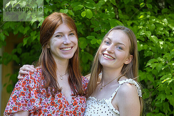 Blondes Teenager-Mädchen mit junger Frau  die vor einer Pflanze steht