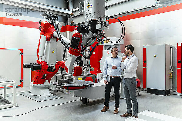 Männliche Automatisierungsingenieure diskutieren mit Maschinen in einer Fabrik