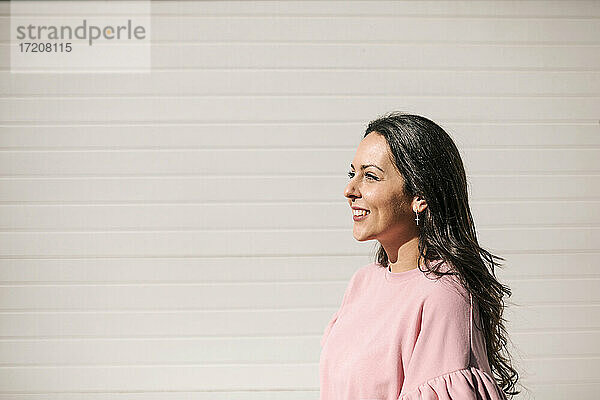Lächelnde Frau an einer Mauer stehend an einem sonnigen Tag