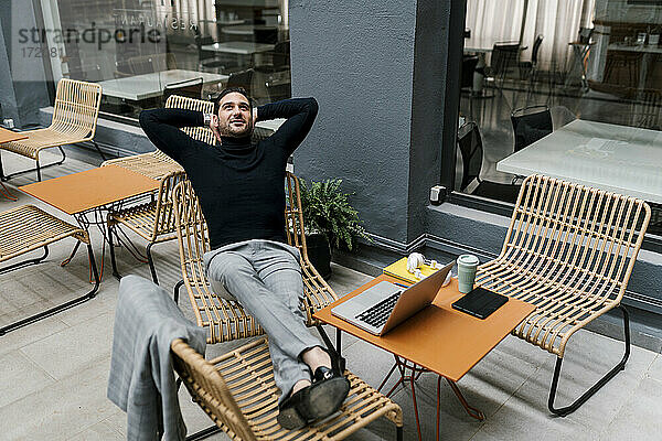Geschäftsmann  der mit übereinander geschlagenen Beinen auf einem Stuhl im Café sitzt und sich entspannt