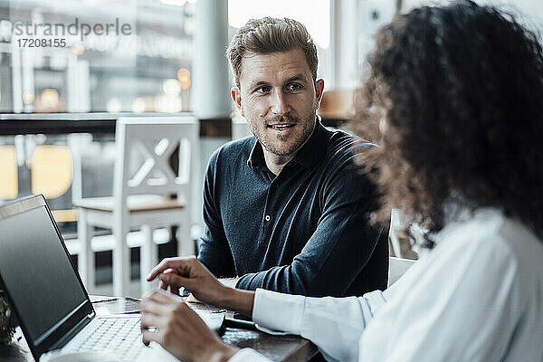 Geschäftsmann bespricht sich mit einem Kollegen  der einen Laptop benutzt  während er in einem Café sitzt