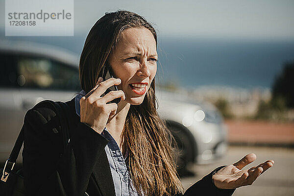 Verärgerte Geschäftsfrau  die an einem sonnigen Tag mit ihrem Mobiltelefon spricht