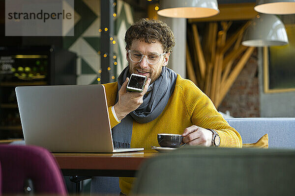 Geschäftsmann  der eine Sprachnachricht über sein Smartphone sendet  während er einen Kaffee im Café trinkt
