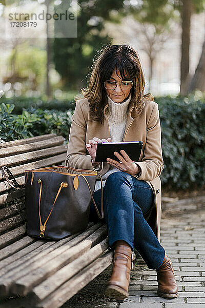 Ältere Frau  die ein digitales Tablet benutzt  während sie auf einer Bank im Park sitzt