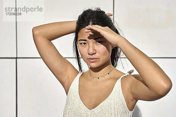 Junge Frau  die ihre Augen zum Schutz vor Sonnenlicht gegen eine Wand abschirmt