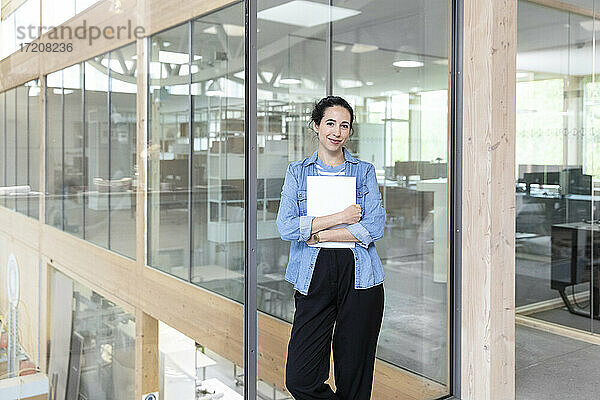 Geschäftsfrau  die ein Dokument hält  während sie gegen eine Glaswand im Büro steht