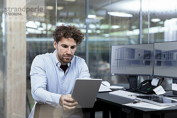 Junger Geschäftsmann  der ein digitales Tablet benutzt  während er am Schreibtisch im Büro sitzt