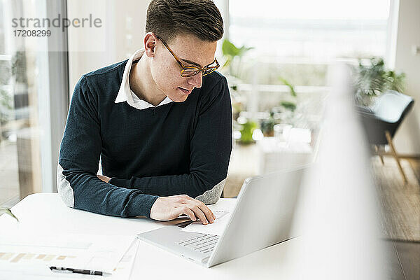 Geschäftsmann mit Brille  der ein Dokument liest  während er am Schreibtisch sitzt