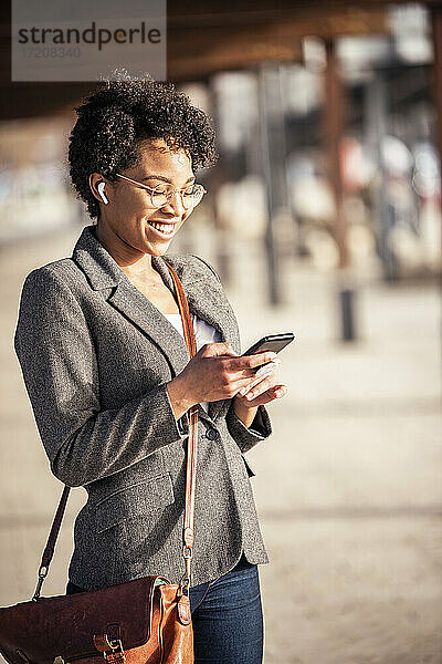 Lächelnde Frau  die auf dem Gehweg ein Mobiltelefon benutzt