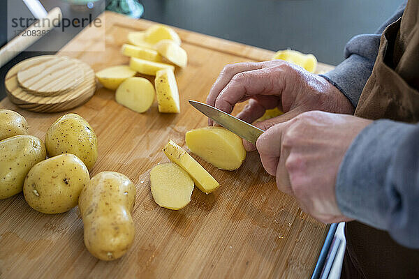 Älterer Mann schneidet rohe Kartoffeln auf einem Schneidebrett in der Küche