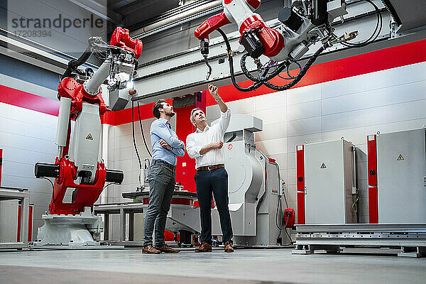 Männlicher Ingenieur erklärt einem Kollegen in einer Fabrik einen Roboterarm