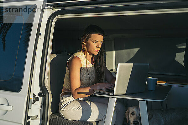 Frau benutzt Laptop  während sie am Wochenende im Wohnmobil sitzt