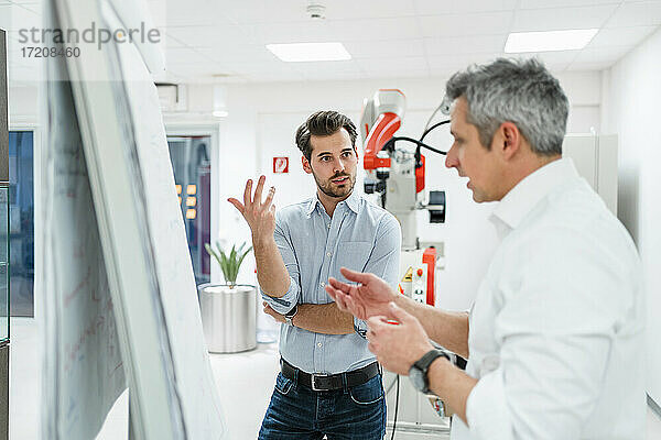 Männliche Ingenieure gestikulieren bei der Diskussion von Geschäftsplänen am weißen Brett in einer Fabrik