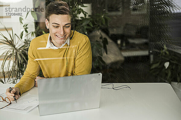 Lächelnder Geschäftsmann im Gespräch per Videokonferenz im Büro zu Hause