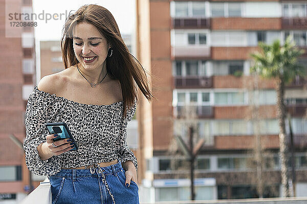 Lächelnde junge Frau  die in der Stadt ein Mobiltelefon benutzt