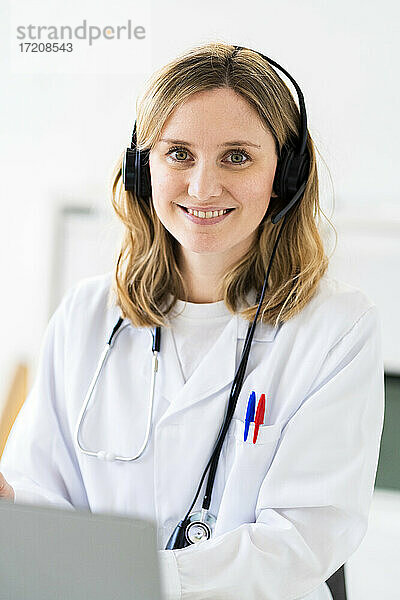 Lächelnde Ärztin mit Kopfhörern während einer Online-Konsultation in einer medizinischen Klinik
